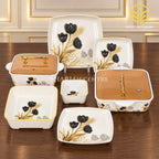 Glamour black tulip dinnerware with square plates, matching bowls and amber-lidded serving dishes is displayed on a wooden table.